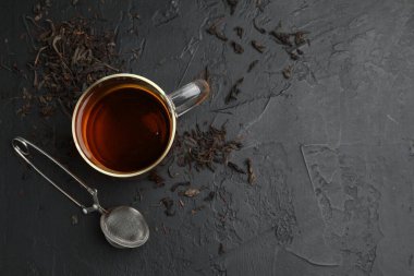 Bir fincan çay, kuru yapraklar ve siyah masada metal infüzyon. Metin için boşluk