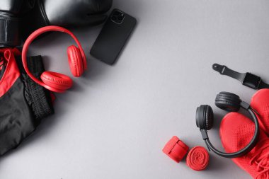 Kulaklıklar, akıllı telefon, saat, spor kıyafetler ve gri arka planda ayakkabılar, düz yatak. Metin için boşluk