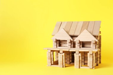 Sarı arka planda tahta bloklardan yapılmış bir ev. Metin için boşluk