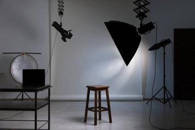 Profesyonel ışıklandırma ekipmanları fotoğraf stüdyosunda tavandan ve sandalyeden sarkıyor.