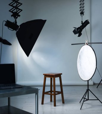 Profesyonel ışıklandırma ekipmanları fotoğraf stüdyosunda tavandan ve sandalyeden sarkıyor.