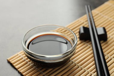 Soya sosu cam kasede ve çubuklar gri masada, yakın plan.