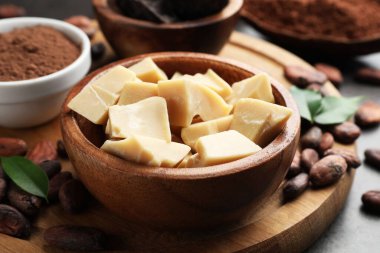 Organik kakao yağı, fasulye, toz ve yeşil yapraklar gri masada, yakın plan.