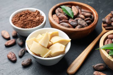 Organik kakao yağı, fasulye, toz ve yeşil yapraklar siyah masada, yakın plan.