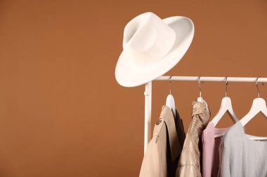 Kahverengi arka planda asılı farklı kıyafetler ve şapkalar, yakın plan. Metin için boşluk