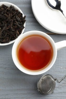 Bir fincan çay, kuru yapraklar ve gri ahşap masada metal aşılayıcı.