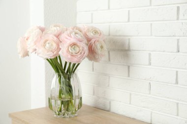 Güzel ranunculus çiçekleri cam vazoda beyaz tuğla duvarın yanındaki tahta çekmece çekmecesinde. Metin için boşluk