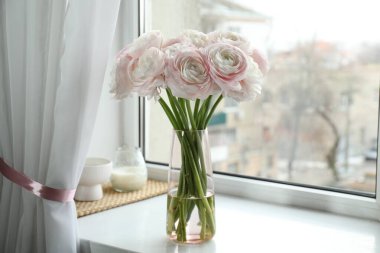 Güzel ranunculus çiçekleri cam vazoda, beyaz pencere eşiğinde.