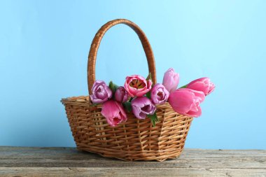 Hasır sepetteki güzel çiçekler ahşap masada açık mavi arka planda