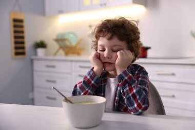 Mutfaktaki beyaz mermer masada lapa yemeyi reddeden mutsuz küçük çocuk.