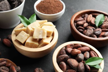 Organik kakao yağı, fasulye, toz ve yeşil yapraklar siyah masada, yakın plan.