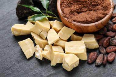 Organik kakao yağı, fasulye, çikolata parçaları, toz ve yeşil yapraklar siyah masada, yakın plan.