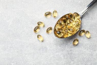 Açık gri masada altın jelatin kapsüllü kaşık, düz. Metin için boşluk