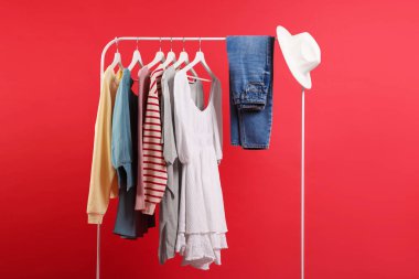 Farklı kıyafetler ve kırmızı arka planda asılı duran şapka.