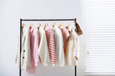 Farklı stil kıyafetler ve çantalar kapalı bir yerde asılı duruyor.