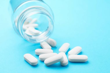 Açık mavi arka planda hapları olan bir ilaç şişesi, yakın plan. Metin için boşluk