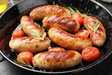 Lezzetli ızgara sosisler, domatesler ve biberiye tavada servis ediliyor. Gri masada, yakın plan.