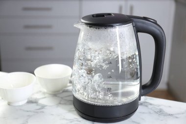 Su elektrikli su ısıtıcısında kaynıyor ve kapılar beyaz mermer masada, yakın plan. Metin için boşluk