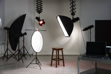 Profesyonel ışıklandırma ekipmanları fotoğraf stüdyosunda tavandan ve sandalyeden sarkıyor.