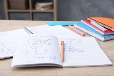Ev ödevi. Tahta masa üzerinde matematik alıştırması ve kırtasiye malzemesi olan defterler, yakın plan.