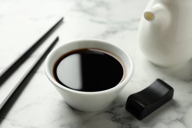 Soya sosu kasede, yemek çubukları ve sürahi hafif mermer masada, yakın plan.