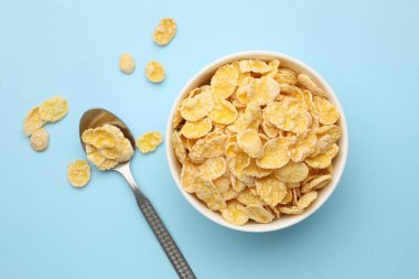 Lezzetli mısır gevrekleri kasede ve kaşıklar açık mavi arka planda, düz uzanmış