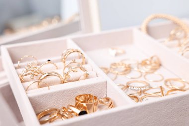 Bulanık gri arkaplan ve seçici odaklanma karşısında farklı altın mücevherlere sahip bej tepsi