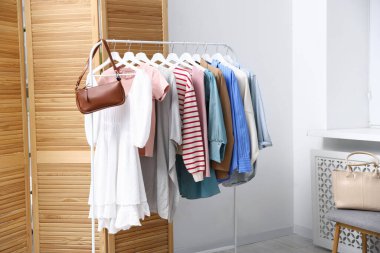 Farklı şık kıyafetler ve çantalar askıda asılı duruyor.