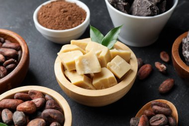 Organik kakao yağı, fasulye, çikolata parçaları, toz ve yeşil yapraklar siyah masada, yakın plan.