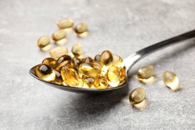 Açık gri masada altın jelatin kapsüllü kaşık, yakın plan.