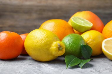 Farklı taze narenciye meyveleri ve yeşil yapraklar gri masada, yakın plan.