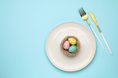 Paskalya kutlaması. Çatal bıçaklı şenlik masası ve açık mavi arka planda boyanmış yumurtalar. Metin için boşluk