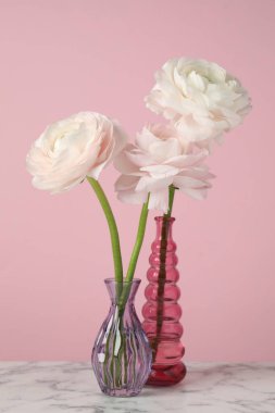 Güzel ranunculus çiçekleri beyaz mermer masada, pembe arka planda, yakın planda.