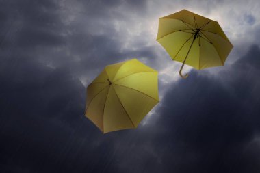 Kara bulutlu gökyüzünde uçan şemsiyeler. Fırtınalı hava