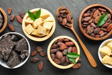 Organik kakao yağı, fasulye, çikolata parçaları ve yeşil yapraklar siyah masanın üzerinde, düz uzanmış