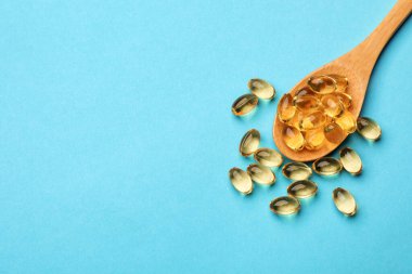 Açık mavi arka planda altın jelatin kapsüllü kaşık, düz. Metin için boşluk