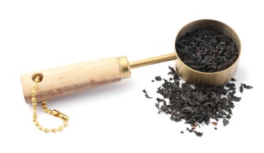 Kurumuş siyah çay yaprakları ve beyazın üzerinde izole edilmiş kaşık ölçüleri.