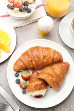 Nefis bir kahvaltı. Reçelli lezzetli kruvasanlar, böğürtlenler, içecekler ve açık gri masada yulaf ezmesi.