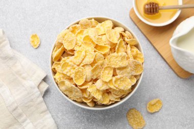 Lezzetli mısır gevrekleri kasede, süt ve bal açık gri arka planda, düz uzanmış