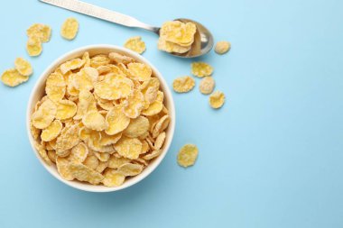 Lezzetli mısır gevrekleri kasede ve kaşıklar açık mavi arka planda, düz yerde. Metin için boşluk