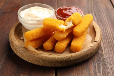 Lezzetli kızarmış peynir çubukları ve soslar ahşap masada, yakın plan.