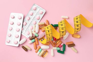 Different pills, measuring tape and blisters on pink background, flat lay