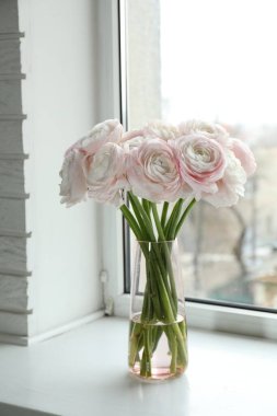 Güzel ranunculus çiçekleri cam vazoda, beyaz pencere eşiğinde.