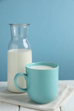 Kupada taze süt ve beyaz ahşap masada sürahi.