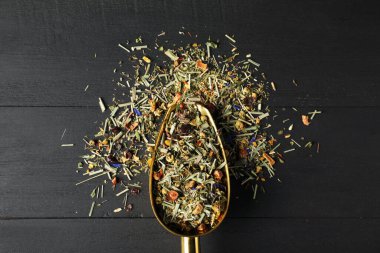 Kurutulmuş bitki çayı yapraklı kepçe siyah ahşap masa, üst manzara.