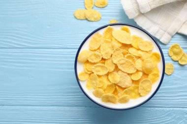 Tasty corn flakes with milk in bowl on light blue wooden table, top view. Space for text