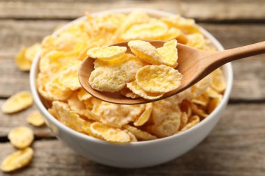 Eating tasty corn flakes with spoon at wooden table, closeup