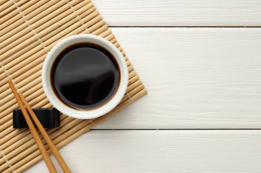 Soy sauce in bowl and chopsticks on white wooden table, top view. Space for text