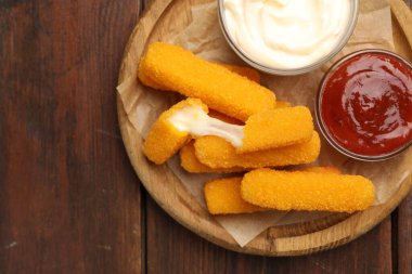 Tasty fried cheese sticks and sauces on wooden table, top view. Space for text