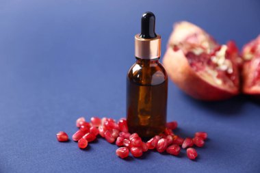 Bir şişe gerekli yağ ve mavi arka planda taze nar, yakın plan.